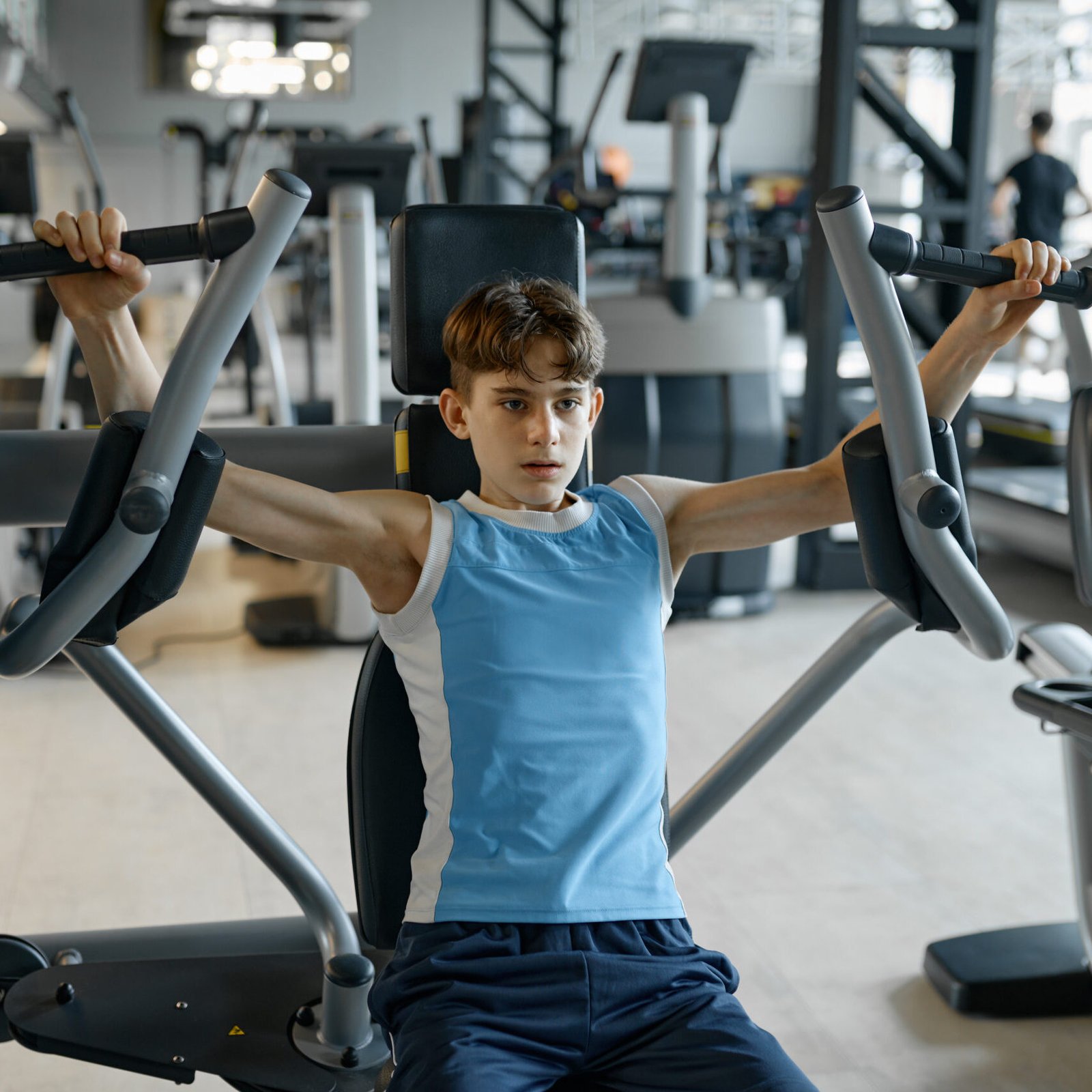 Active teenager boy doing physical exercise training at sports gym equipment. Children masculinity development