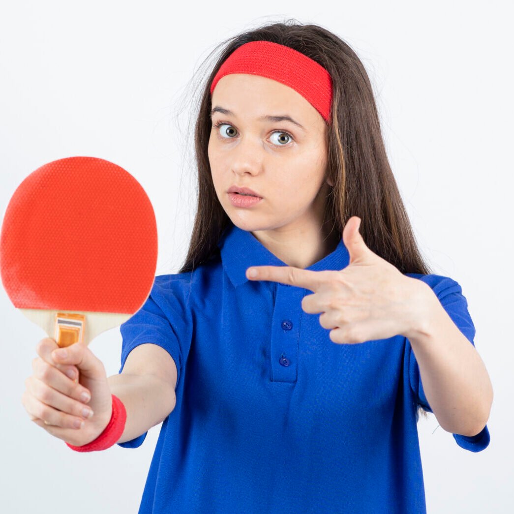 Photo of a young girl pointing at table tennis racket over a white wall . High quality photo