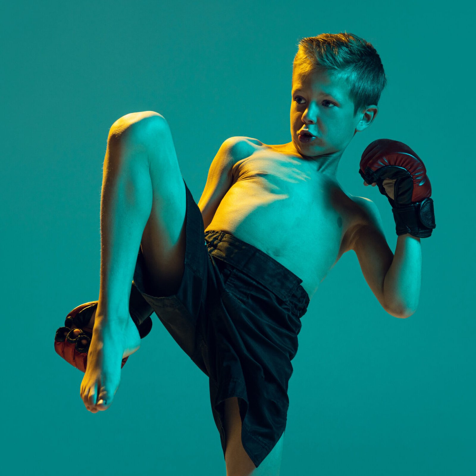 Portrait of little boy, kid in gloves training, practicing thai boxing on green studio background in neon light